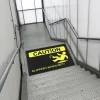 Čierna rohož JET PRINT HI-VIS so žltým symbolom pošmyknutia a nápisom CAUTION na schodiskovej podeste