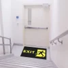 Čierna rohož JET PRINT HI-VIS so žltým nápisom EXIT a symbolom východu pred dverami na schodiskovej podeste