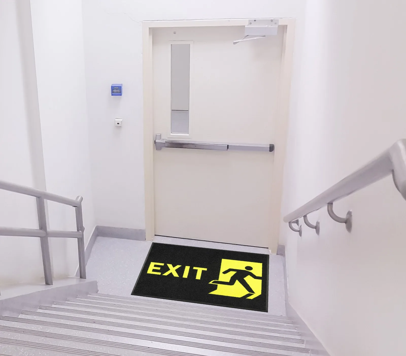 Čierna rohož JET PRINT HI-VIS so žltým nápisom EXIT a symbolom východu pred dverami na schodiskovej podeste