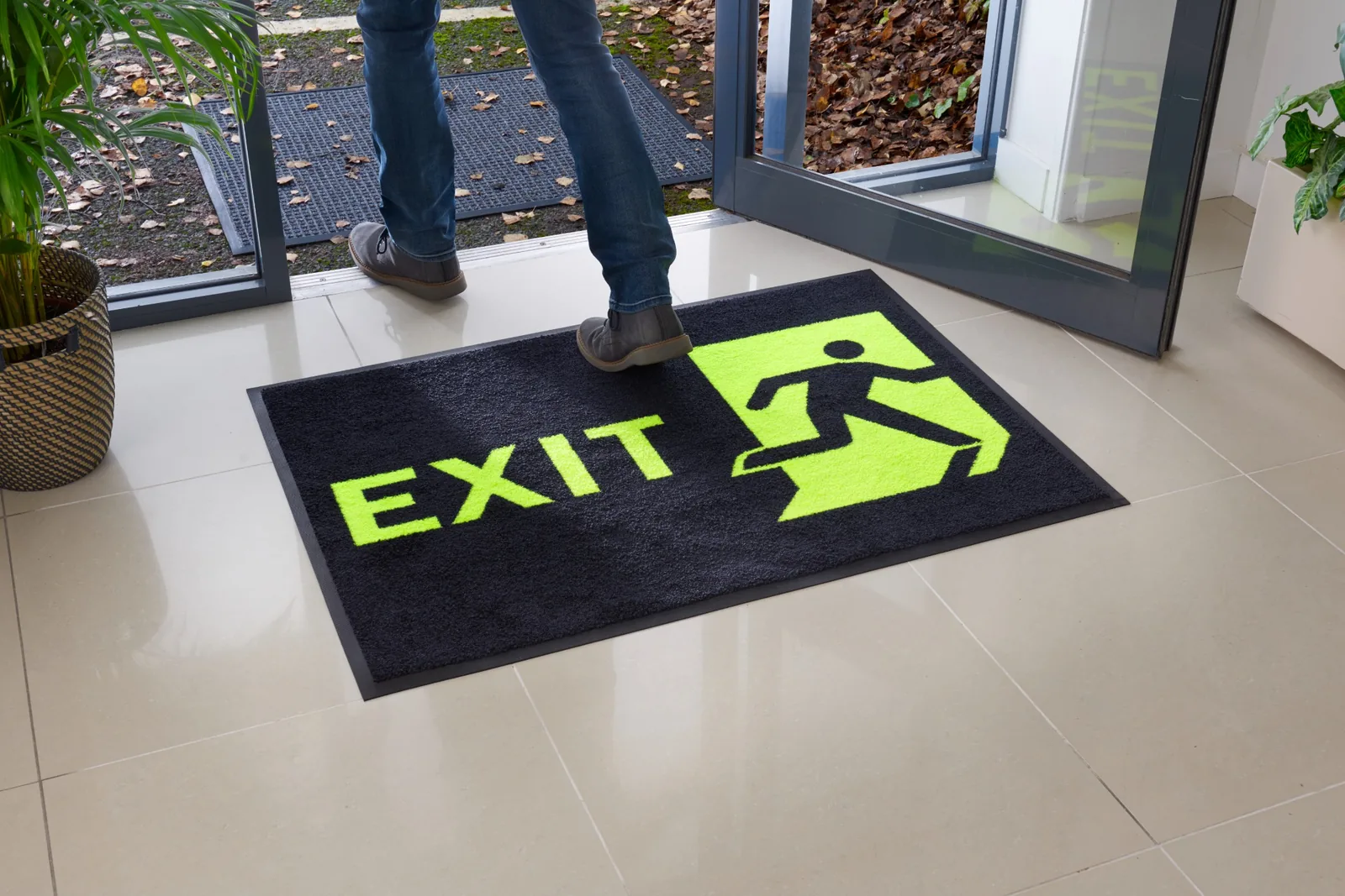 Čierna rohož JET PRINT HI-VIS so žltým nápisom EXIT a symbolom východu pri otvorených presklených dverách