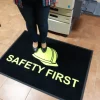Človek stojaci na čiernej rohoži JET PRINT HI-VIS so žltou prilbou a nápisom SAFETY FIRST pri zariadení