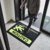 Rohož JET PRINT HI-VIS s nápismi CAUTION a SLIPPERY WHEN WET pod človekom pri presklenom vstupe