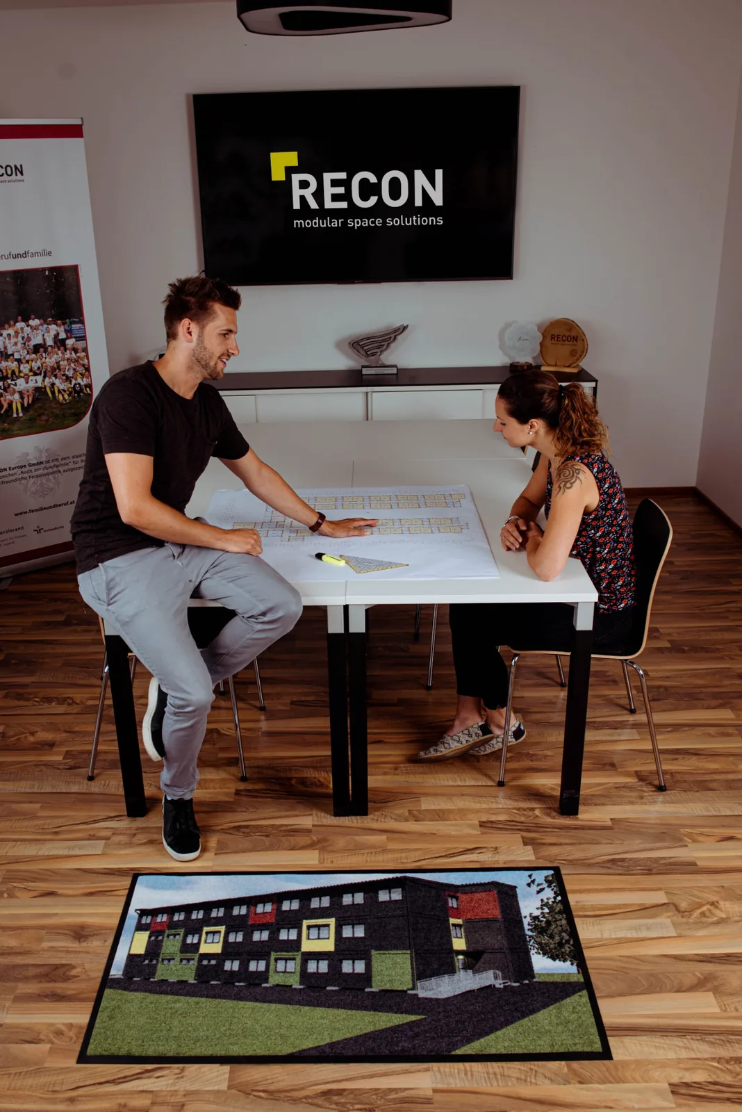 Rohož JET PRINT PATIO s farebnou grafikou budovy a logom RECON pred stolom v kancelárii
