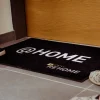 Čierna rohož JET PRINT PATIO s bielym nápisom @HOME a logom REHOME pred dverami