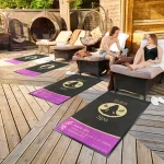 Čierne a fialové rohože JET PRINT PATIO s logom pred oddychovými ležadlami na drevenej terase