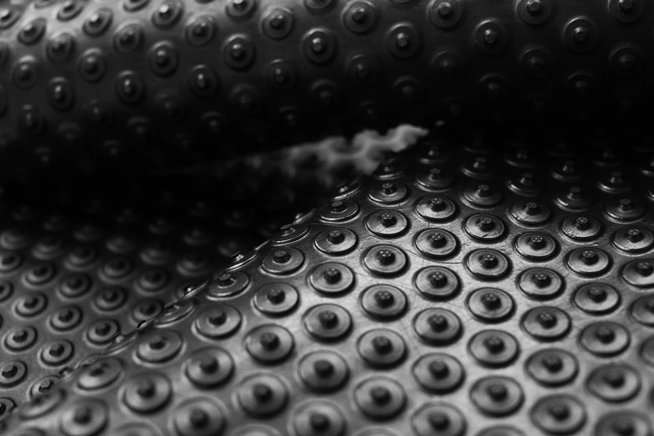 Detail ohnutej čiernej rohože KLEEN COIL s pravidelnými kruhovými výstupkami