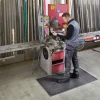 Pracovník stojaci na čiernej rohoži KLEEN COIL pri obsluhe stroja vo výrobnom priestore