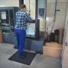 Pracovník stojaci na čiernej rohoži KLEEN COIL pri ovládacom paneli stroja