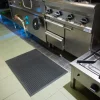 Čierna profilovaná rohož KLEEN CUSHION na dlažbe pred nerezovými sporákmi v kuchyni